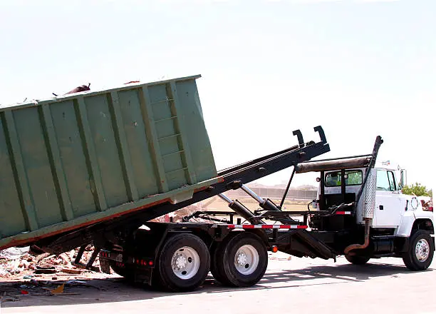 A dumpster loaded with trash is unloaded by a heavy duty truck.